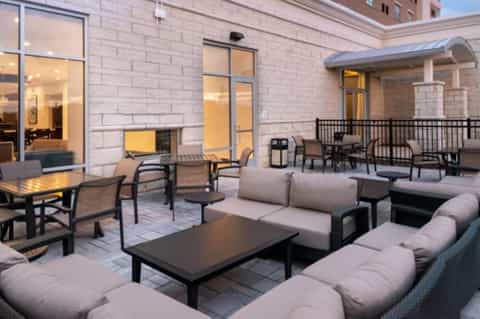 Outdoor patio with lounge seating, fire pit, dining tables, and modern building exterior at dusk