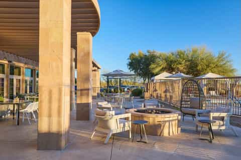 Desert resort courtyard with fire pit seating, umbrellas, architectural columns, and desert landscaping