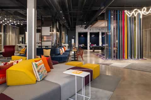 Modern hotel lounge with yellow modular seating, colorful accent pillows, dark blue furniture, and vibrant neon signage