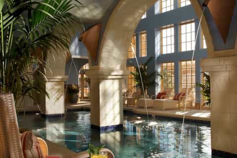 Indoor spa or pool area with arched ceilings, columns, tropical plants, and natural light streaming in
