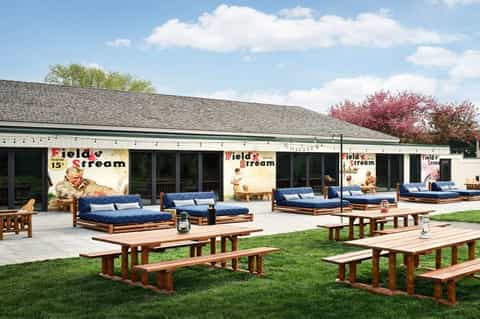 Field & Stream outdoor patio with wooden picnic tables, blue cushioned lounge chairs, and vintage signage