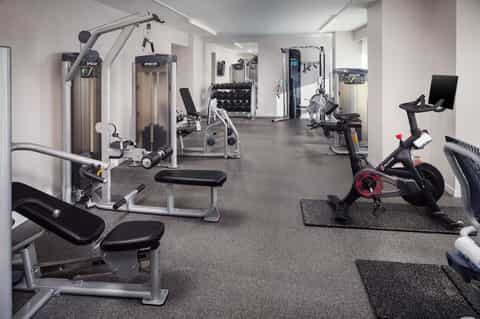 Spacious fitness center with cardio machines, weight equipment, exercise bikes, and dumbbells on gray flooring