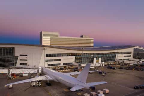 Commercial aircraft parked at airport terminal gate with modern hotel building illuminated at dusk