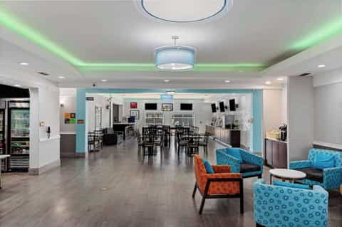 Modern hotel lobby with bright seating area, dining tables, and green accent lighting on ceiling