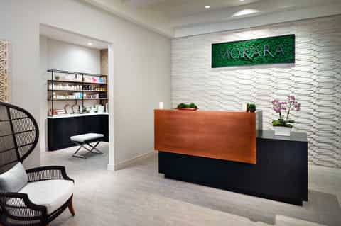 Modern spa reception area with orange desk, white textured walls, green moss wall art, and minimalist design