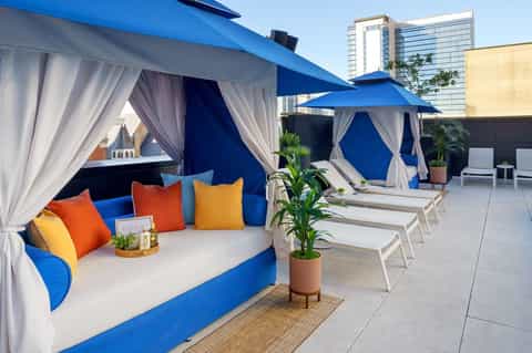 Rooftop lounge area with blue cabanas, white curtains, colorful pillows, and city skyline views
