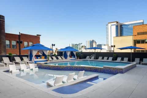 Rooftop pool with blue umbrellas, white lounge chairs, and city skyline in background