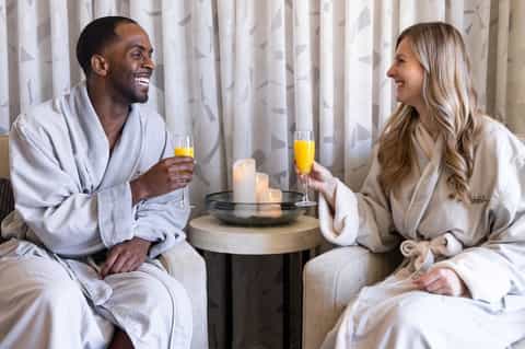 Couple in white robes toasting with champagne by candlelight in elegant room setting