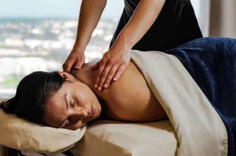 Professional massage therapist performing shoulder massage on client with city view
