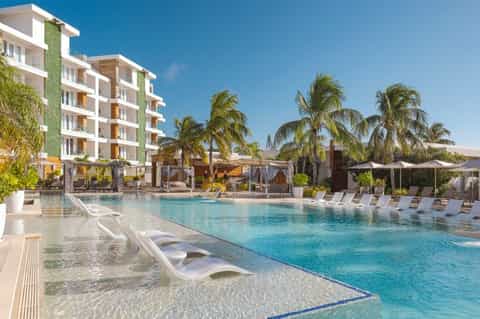 Modern resort pool with shallow entry, palm trees, white building with green accent wall