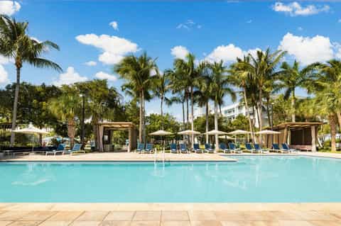 Resort pool surrounded by palm trees, lounge chairs, and wooden cabanas