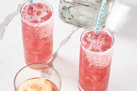 Two glasses of pink cocktails with silver rum bottle on marble countertop