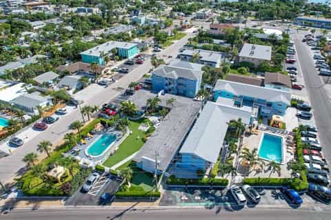 Aerial view of modern resort complex with pools, turquoise buildings, and palm trees surrounded by parking