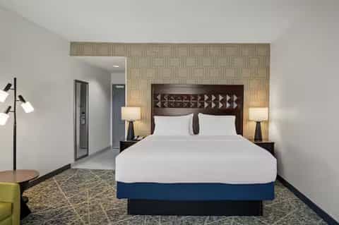 Hotel bedroom with queen bed, geometric headboard, patterned wallpaper, and modern furnishings