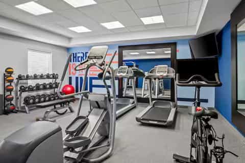 Hotel fitness center with cardio equipment, dumbbells, exercise bike, and motivational wall signage