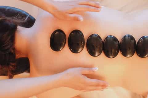 Hot stone massage therapy with black basalt stones applied to client's back for therapeutic treatment