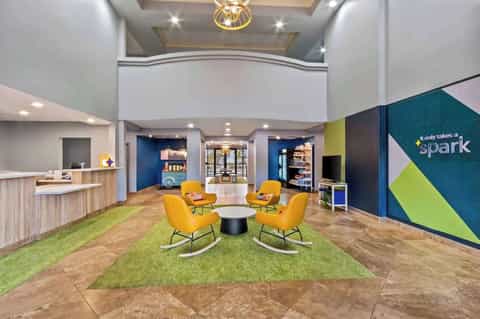 Modern hotel lobby with yellow accent chairs, green carpet, blue walls, and reception desk with contemporary lighting fixtures