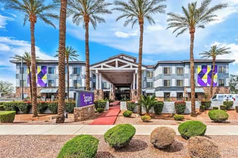 Contemporary hotel exterior with white and gray facade, purple geometric patterns, palm trees, and red entrance walkway
