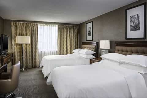 Hotel double room with two queen beds, patterned curtains, desk, and traditional furnishings in neutral tones