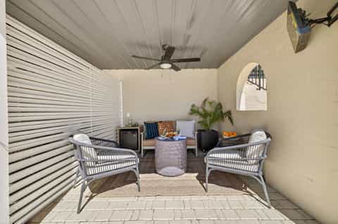 Covered patio lounge area with wicker chairs, potted plants, and modern furniture facing a stucco wall