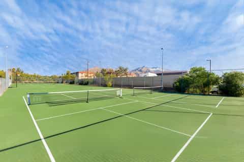 Multiple professional tennis courts with white line markings and net posts under blue sky
