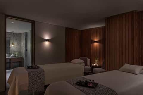 Luxury spa bedroom with dual beds, wood paneling, soft lighting, and ensuite bathroom