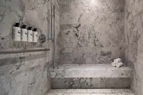 Marble spa shower with premium toiletries and rolled white towels on bench