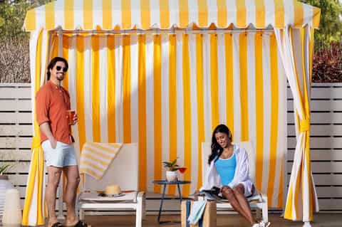 Couple relaxing in yellow and white striped cabana with lounge chairs and small table