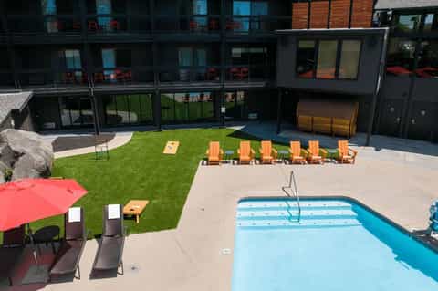 Aerial view of modern resort with lap pool, lawn area, orange lounge chairs, and red umbrellas