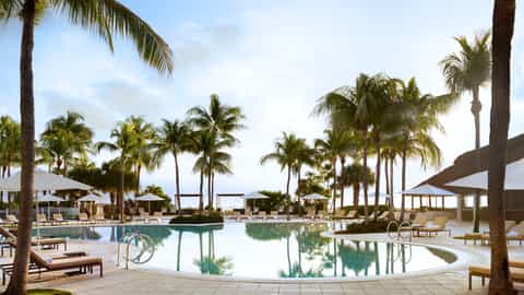 Large lagoon-style pool surrounded by white umbrellas, palm trees, and modern resort structures
