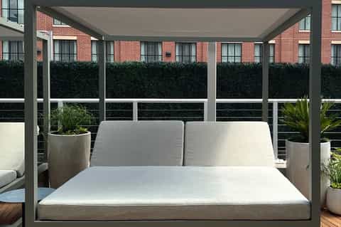 Modern gray pergola daybed with white cushions on rooftop terrace with city views