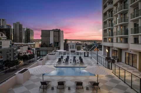 Rooftop pool at dusk with pink sunset sky, striped umbrellas, and city skyline backdrop