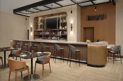 Modern lounge bar with wooden bar counter, seating area, and illuminated shelving