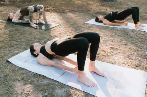Outdoor yoga class with three people performing exercises on white mats on dirt ground