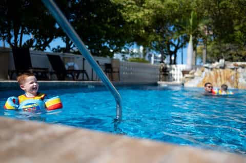 Young child in yellow flotation device playing in pool with adult nearby