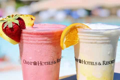 Two colorful poolside cocktails in Omni Hotels & Resorts branded glasses with fruit garnish