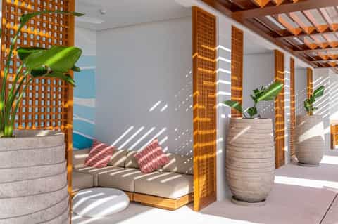 Modern spa lounge with wooden lattice screens, potted plants, beige seating, and natural light streaming through skylights