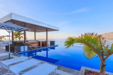Infinity pool with cabana, palm tree, and mountains visible across tranquil blue water
