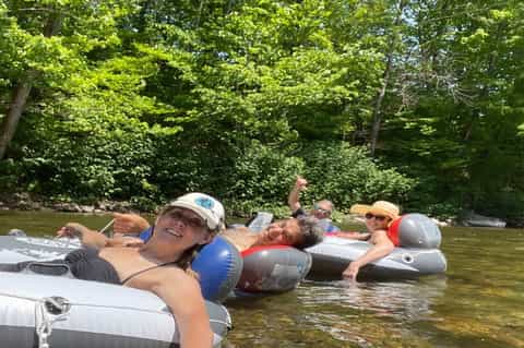 Group of people floating on inflatable tubes down a calm river surrounded by green trees and vegetation