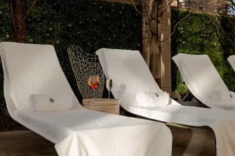 White lounge chairs with small pillows under pergola against ivy-covered wall in spa setting