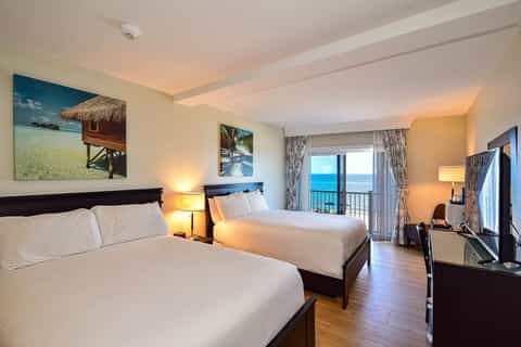 Modern hotel room with two queen beds, ocean view balcony, and tropical wall art décor