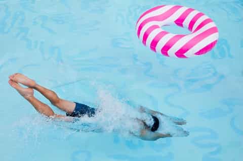 Swimmer doing freestyle stroke in pool with pink and white striped inflatable float nearby