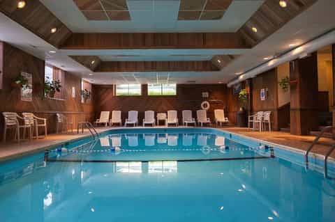 Indoor heated swimming pool with lane dividers, wooden walls, and lounge chairs in athletic facility