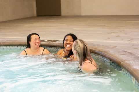 Three women relaxing and smiling in indoor hot tub with wooden surround