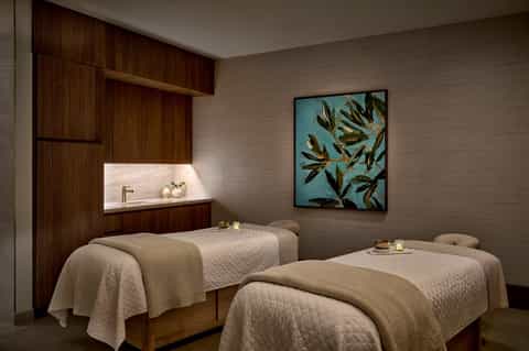 Spa treatment room with two massage beds, wooden accents, artwork, and ambient lighting