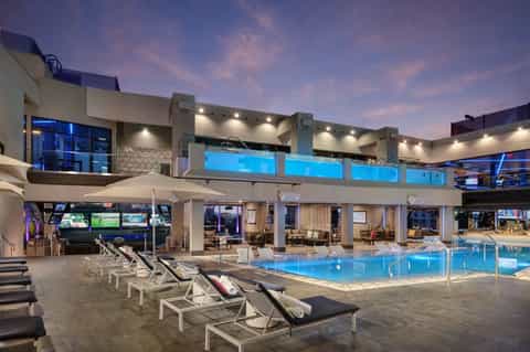 Upscale resort pool at dusk with lounge chairs, modern architecture, and lit buildings