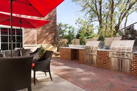 Brick patio with outdoor dining furniture, red umbrella, and built-in stainless steel grill