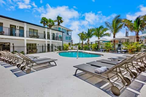 Modern apartment building with curved pool, lounge chairs, and white umbrellas in sunny courtyard