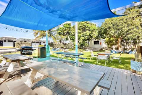 Outdoor picnic area with tables under blue shade sail, grill, and landscaped lawn