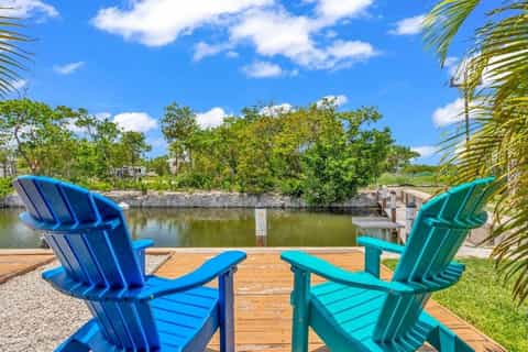 Blue and teal Adirondack chairs on wooden deck overlooking calm waterway with mangroves